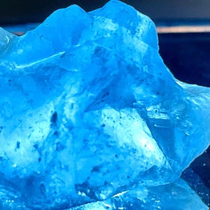 May include: A large, clear blue crystal with a rough, irregular shape. The crystal is translucent and has a slight shimmer.