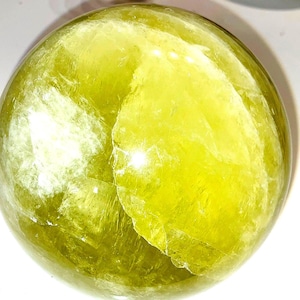 May include: A translucent, spherical object with a vibrant yellow-green hue. The sphere has a textured, layered appearance, with visible internal patterns. The object is likely a decorative item or a natural stone, possibly a crystal ball.