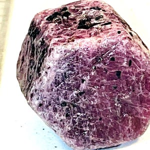 Peut inclure: Une grosse pierre précieuse de rubis rose brute avec des inclusions noires. Le rubis mesure environ 3,8 cm de diamètre.