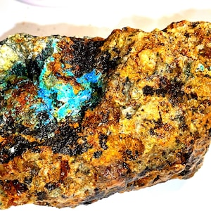 Könnte beinhalten: Ein rauer, brauner und schwarzer Stein mit einem Fleck aus leuchtend blauen und grünen Kristallen.