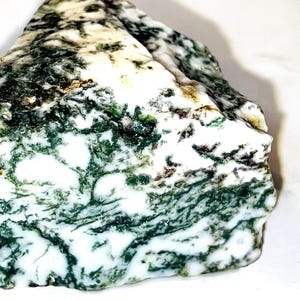 May include: A large, irregularly shaped piece of moss agate with a white base and green moss-like patterns. The stone has a rough, natural texture.