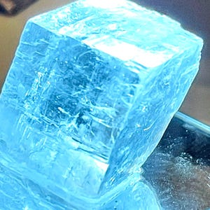 May include: A large, clear blue cube with a textured surface. The cube is sitting on a black surface.