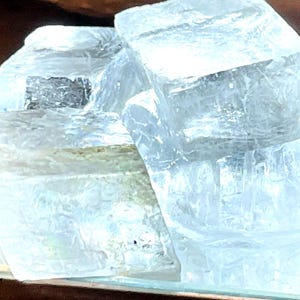 May include: A collection of translucent, pale blue selenite crystals. The crystals are arranged in a layered, blocky formation, with visible internal structures. The arrangement suggests a natural formation, possibly for decorative or metaphysical purposes.