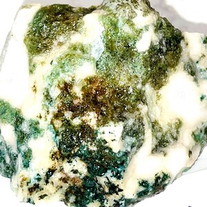 May include: A rough, white rock with green and brown inclusions. The rock has a mottled appearance and is about 7 cm in diameter.