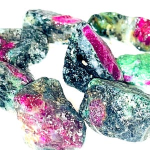 May include: A collection of rough, uncut ruby in zoisite gemstones. The stones are a mix of dark green, black, and pink.