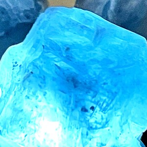 May include: A large, translucent blue crystal with a rough, textured surface. The crystal is illuminated from within, creating a soft, glowing effect.