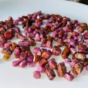 May include: A close-up of a pile of pink and brown rough gemstones on a white surface.