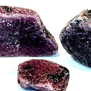 Può includere: Tre pietre preziose di rubino grezze e naturali. I rubini sono di un colore rosso porpora intenso e hanno una superficie grezza non lucidata.