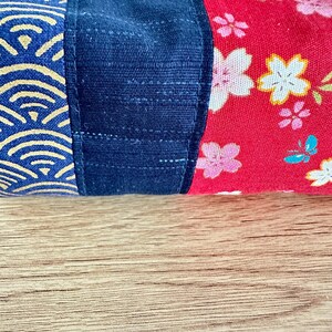 May include: Close-up of a fabric item with three distinct sections. The first section features a blue and gold wave pattern. The middle section is a solid dark blue. The final section is red with white and pink floral designs.