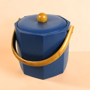 Puede incluir: Una cubitera octogonal de color azul oscuro con una tapa a juego que presenta un pomo redondo de madera. El recipiente incluye un asa giratoria curva de color marrón claro, estilo bambú, fijada a los lados para un agarre funcional.