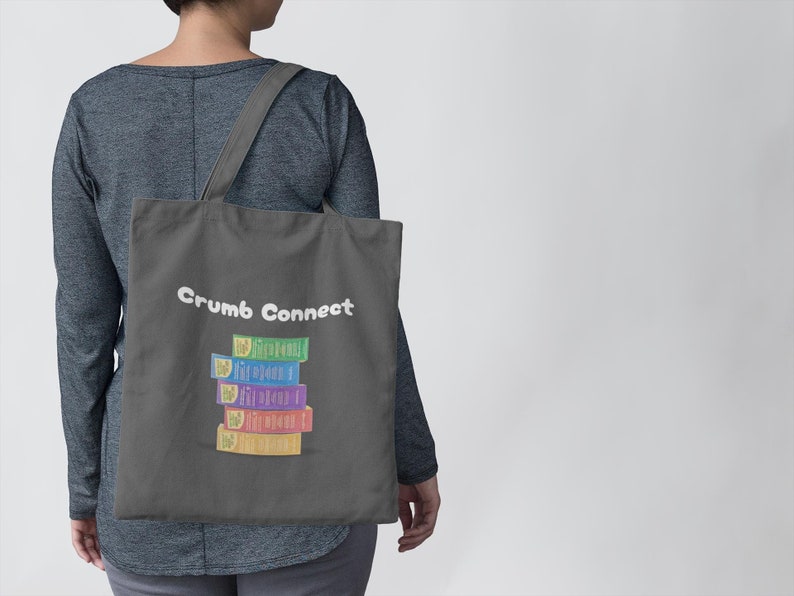 May include: A gray tote bag with the text "Crumb Connect" printed in white. A stack of colorful boxes with the text "The First Bread" printed on each box is centered on the bag.