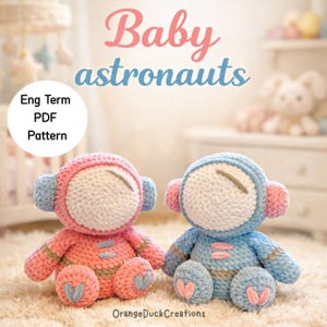 Könnte beinhalten: Zwei gehäkelte Baby-Astronauten-Puppen, eine rosa und eine blaue, sind nebeneinander zu sehen. Jede Puppe hat ein weißes Gesicht, rosa oder blaue Ohrenschützer und einen passenden Körper. Der Text "Baby astronauts" steht über den Puppen.