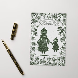 May include: A greeting card with a green illustration of a mother and child figure, surrounded by floral elements. The card reads "To The Greatest Mother For Always Being Near." A black and gold pen is next to the card.