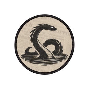 以下が含まれることがあります： 水から現れる黒い蛇のデザインが施された丸いパッチ。蛇は長く湾曲した首と詳細な鱗状の体を持っています。背景は明るいタン色で、パッチには黒い縁取りがあります。