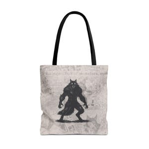 May include: Tote bag with a black and white illustration of a werewolf. The bag has black handles and a light gray background with newspaper-style text. The text in the image reads "Michigan: Full of monsters, myths."
