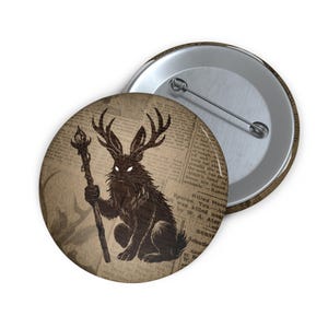 Pode incluir: Um botão com uma ilustração marrom escuro de um coelho com chifres, segurando um bastão com uma chama. O fundo é uma impressão de jornal vintage. O botão é redondo com uma parte traseira de metal.
