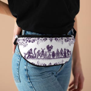 Può includere: Un marsupio bianco con una stampa grafica viola di vari criptidi e creature mitiche disposti in fila, incorniciati da un bordo floreale decorativo lungo i bordi superiore e inferiore, con chiusura a zip nera e cinturino nero.