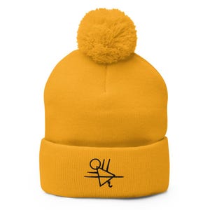 May include: A yellow beanie with a black pom pom and a black embroidered design on the front. The design is a triangle with a circle and lines.