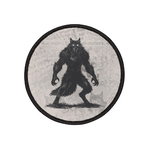 May include: Round patch featuring a black werewolf illustration with glowing white eyes, standing on grass. The background is a faded newspaper print. The patch has a black border.