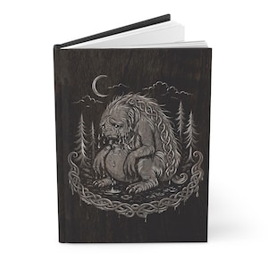 May include: A hardback journal with a dark wood-grain cover. The cover features a detailed illustration of a sad, furry creature with a Celtic knot design, surrounded by trees, a moon, and clouds. The creature is weeping.