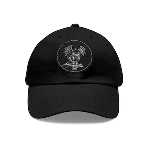 May include: Black baseball cap with a circular patch depicting a detailed illustration of a gargoyle with red eyes and large wings. The patch is stitched onto the front of the cap, creating a striking contrast.