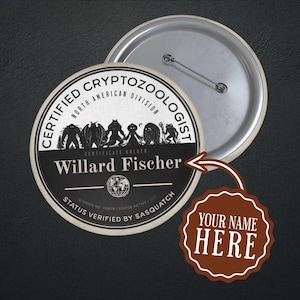 Può includere: Una spilla rotonda con il testo CERTIFIED CRYPTOZOOLOGIST NORTH AMERICAN DIVISION e STATUS VERIFIED BY SASQUATCH. Presenta sagome di creature mitiche, un'icona a forma di globo e il nome Willard Fischer scritto in bianco.