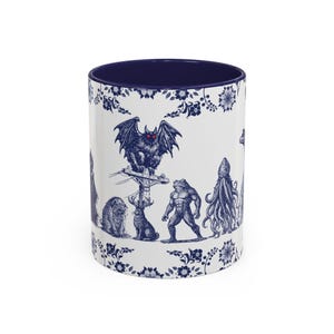May include: White ceramic mug with a navy blue interior and a decorative floral border. The mug features a detailed blue illustration of various mythical creatures, including a bat, frog, and octopus.