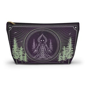 May include: A dark purple zippered pouch featuring a central circular emblem with a hooded figure in a Celtic knotwork robe. The design includes pale green pine trees, a crescent moon, and stars against a deep purple background with rays.