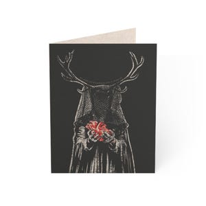 Puede incluir: Tarjeta de felicitación con una ilustración en blanco y negro de una figura con cuernos de ciervo y una cabeza velada, sosteniendo un corazón rojo. La tarjeta tiene el texto "WE BEAR THE WILDERNESS AND IT WEARS US" en la parte superior.