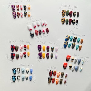 May include: A selection of painted artificial nails with diverse designs. The nails display a variety of colours, including red, blue, gold, and black, with patterns such as hearts, geometric shapes, and abstract art. Each set is labelled with a name.