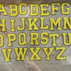 May include: A set of 26 yellow felt letter patches, each letter of the alphabet is individually displayed on a wooden surface.