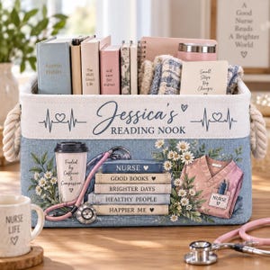 Puede incluir: Una cesta de almacenamiento rectangular de tela con asas de cuerda, que presenta el texto 'Jessica's READING NOOK' y un gráfico de una casaca médica rosa, un estetoscopio, una taza de café y una pila de libros etiquetados 'NURSE', 'GOOD BOOKS', 'BRIGHTER DAYS', 'HEALTHY PEOPLE', 'HAPPIER ME'.