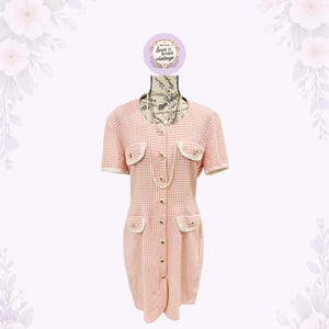 May include: A vintage pink and white gingham dress with short sleeves, a button-down front, and small pockets. The dress has white trim and gold buttons. A long pearl necklace is draped on the mannequin. The text "love is rare vintage" is on a circular tag.