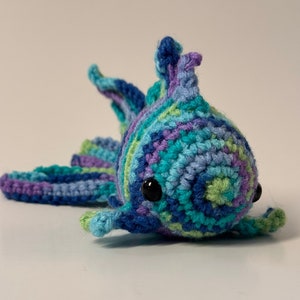 May include: A crocheted blue, green, and purple fish toy with black eyes.