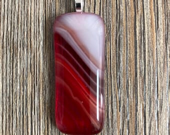 May include: A rectangular fused glass pendant featuring a smooth, polished surface with swirling layers of deep red, translucent white, and soft pink. The pendant is topped with a silver-toned metal bail for hanging, creating a sleek, glossy appearance.