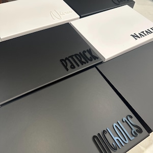May include: Stack of black and white gift boxes with names printed on the top. The names are Patrick, Nicholas, Natalie, and Vina.