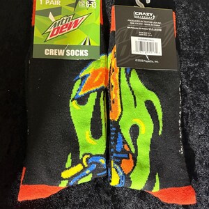 May include: Pair of black crew socks with a colorful graphic design. The socks feature the Mountain Dew logo and the text "CREW SOCKS". The socks are size 6-13.