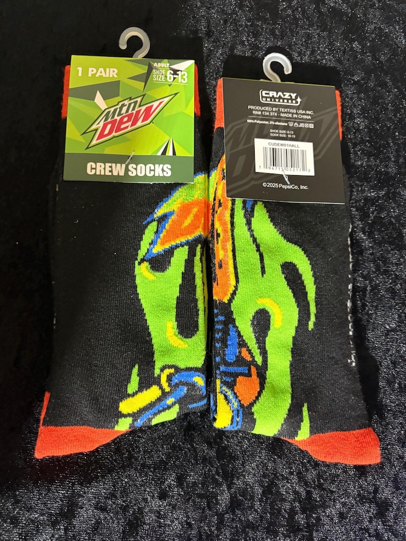 May include: Pair of black crew socks with a colorful graphic design. The socks feature the Mountain Dew logo and the text "CREW SOCKS". The socks are size 6-13.