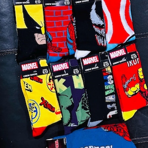 May include: A collection of ten pairs of colorful crew socks featuring Marvel characters. The socks are displayed on a black leather surface. The socks feature characters such as Wolverine, Spiderman, Venom, Iron Man, Hulk, and Deadpool. The socks are all size 9-13.
