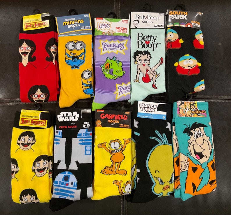 May include: Eleven pairs of crew socks featuring various cartoon characters.  The socks are in yellow, red, purple, black, teal, and light green.  Character themes include Bob's Burgers, Minions, Rugrats, Betty Boop, South Park, Star Wars, Garfield, and The Flintstones.  Sock packaging displays character names and 'socks' or 'crew socks'.