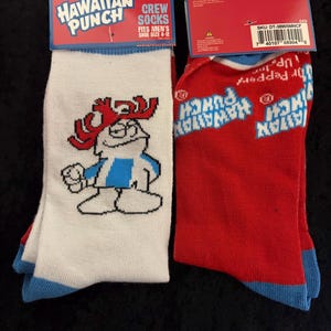 May include: Two pairs of crew socks featuring the Hawaiian Punch logo. One pair is white with a cartoon character and blue accents. The other pair is red with the Hawaiian Punch logo. Both pairs have blue cuffs and are labeled "Fits Men's Shoe Size 6-12."