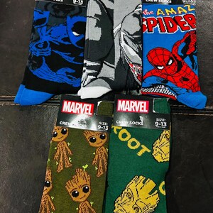 May include: Five pairs of Marvel crew socks featuring different characters. The socks are all size 9-13. The characters featured are Venom, Spider-Man, Groot, and the Infinity Gauntlet.