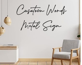 May include: Black metal sign with the text "Custom Words Metal Sign" in a cursive font. The sign is hanging on a white wall in a room with a wooden floor and a chair.