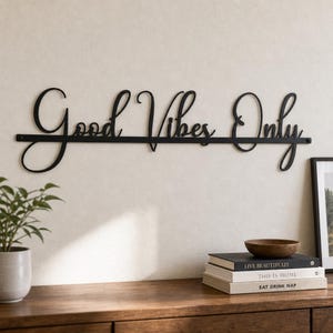 May include: A black metal wall sign featuring the cursive script text Good Vibes Only. The letters are connected by a horizontal line that runs through the center of the phrase, creating a single, continuous piece of wall decor.