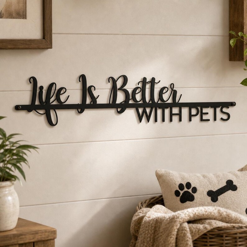 May include: A black metal wall sign featuring the cursive and block text "Life Is Better WITH PETS" mounted horizontally. The sign consists of a thin horizontal bar with the words "Life Is Better" in script above and "WITH PETS" below.