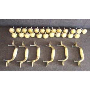 May include: A collection of vintage cabinet hardware, including brass-toned handles with cream-colored inserts and matching round knobs. The handles are curved with screw attachments, and the knobs have a flat, circular design.