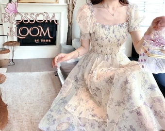 以下が含まれることがあります： 花柄のプリントが施された白いドレスで、スクエアネックラインです。ドレスはパフスリーブとティアードスカートが付いています。ドレスは軽量な生地で作られており、夏の日に最適です。