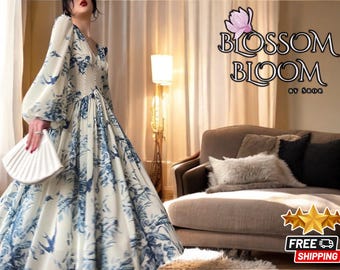 Puede incluir: Una mujer lleva un vestido de estampado floral blanco y azul con mangas largas y falda fruncida. El vestido tiene un escote en V y un corpiño ajustado. La mujer lleva un bolso de mano blanco. El fondo es una pared de color marrón claro con una lámpara y un sofá.