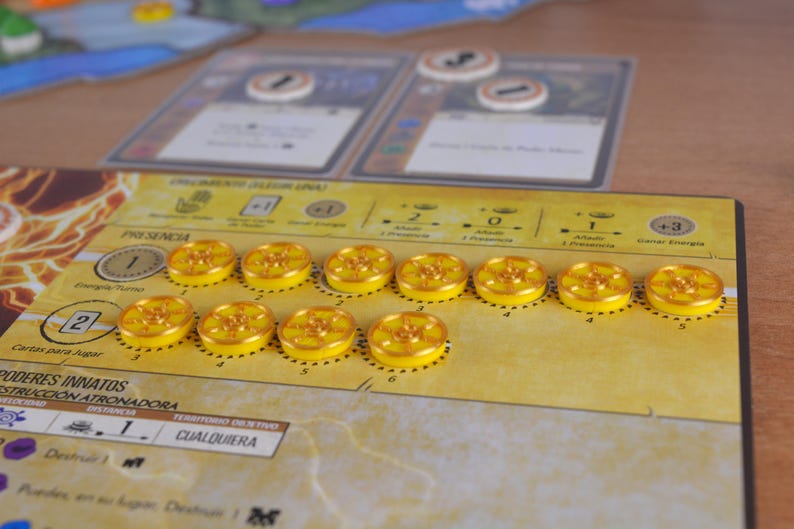 May include: A board game setup with yellow tokens and cards. The game board is tan with text and graphics. The tokens are circular with a yellow center and a gold rim. Two cards are in the background.