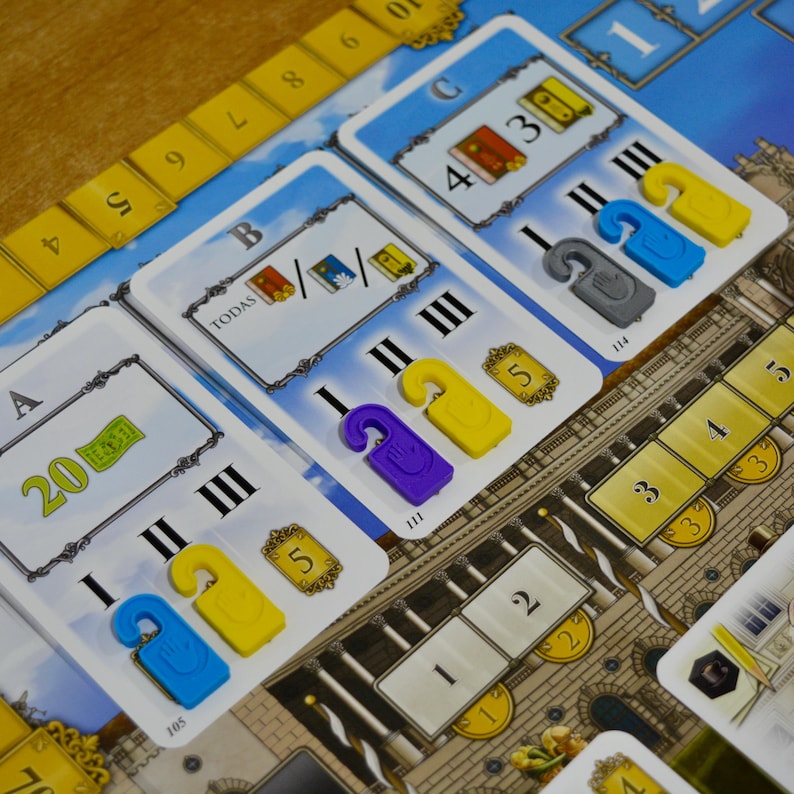 May include: A board game with cards and colorful game pieces. The cards have numbers, illustrations, and text. The game pieces are shaped like hotel door hangers in yellow, blue, purple, and gray. The game board has a cityscape design and a yellow scoring track.